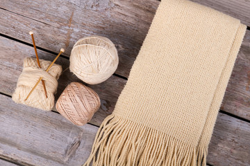Beige knitted scarf with fringe on wooden background.