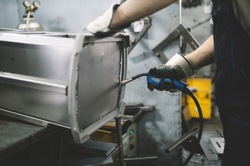Factory for production of heavy pellet stoves and boilers. Close up shot of manual worker's hand welding some parts.