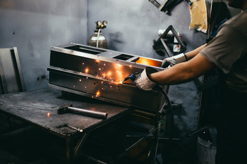 Factory for production of heavy pellet stoves and boilers. Close up shot of manual worker's hand welding some parts.