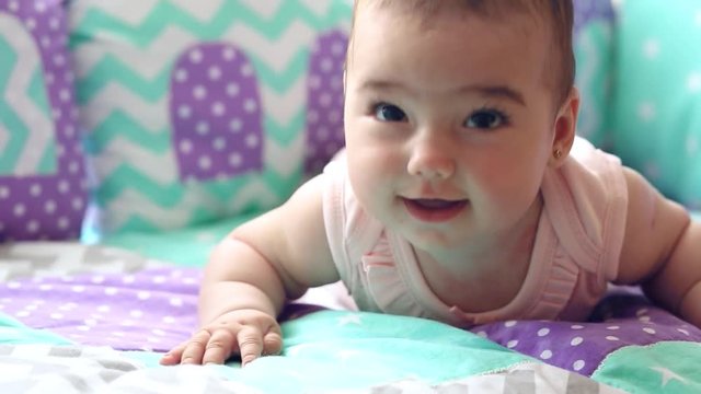 Beautiful happy little girl lying in a crib on his stomach and laughs