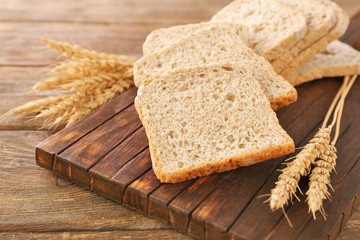 Fototapeta na wymiar Sliced bread with wheat spikes on wooden table closeup