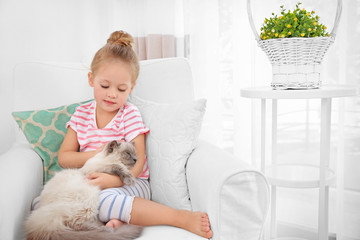 Cute little girl sitting in armchair with fluffy cat