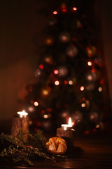 dark photo in brown tones. soft focus tree in multi-colored lights, in front of mandarin and red berries on the branches. Christmas, New Year's mood and atmosphere.
