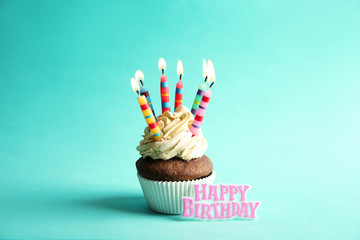 Tasty cupcake with candles and words HAPPY BIRTHDAY on turquoise background