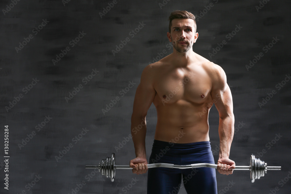 Wall mural Sporty man doing exercises with barbell on dark background