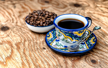 Organic coffee grains and a colorful hand painted coffee cup over wood table