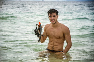 Young muscular handsome man in swimming pants holding diving mask and looking at camera.