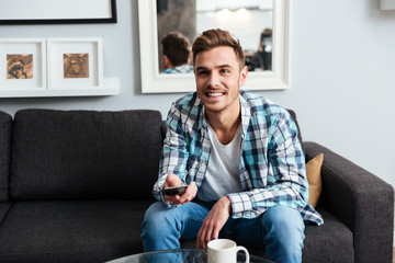 Fototapeta premium Joyful young bristle man holding remote control while watching TV.
