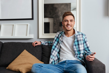 Fototapeta premium Young smiling man sitting on sofa in home while chatting