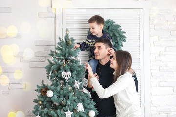 Family of mother, father and little child near Christmas tree with presents, decorations and New Year or Christmas