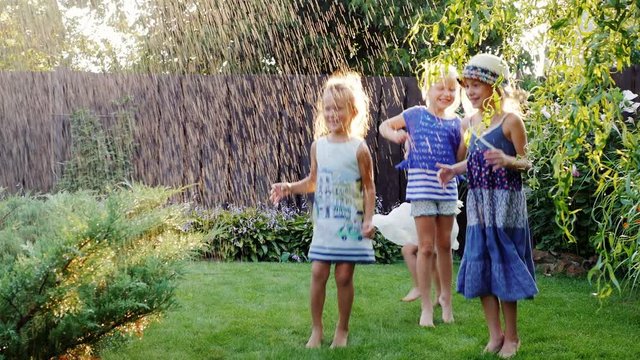 Four carefree cheerful children laughing in the garden under a spray of water. Concept - friendship and childhood