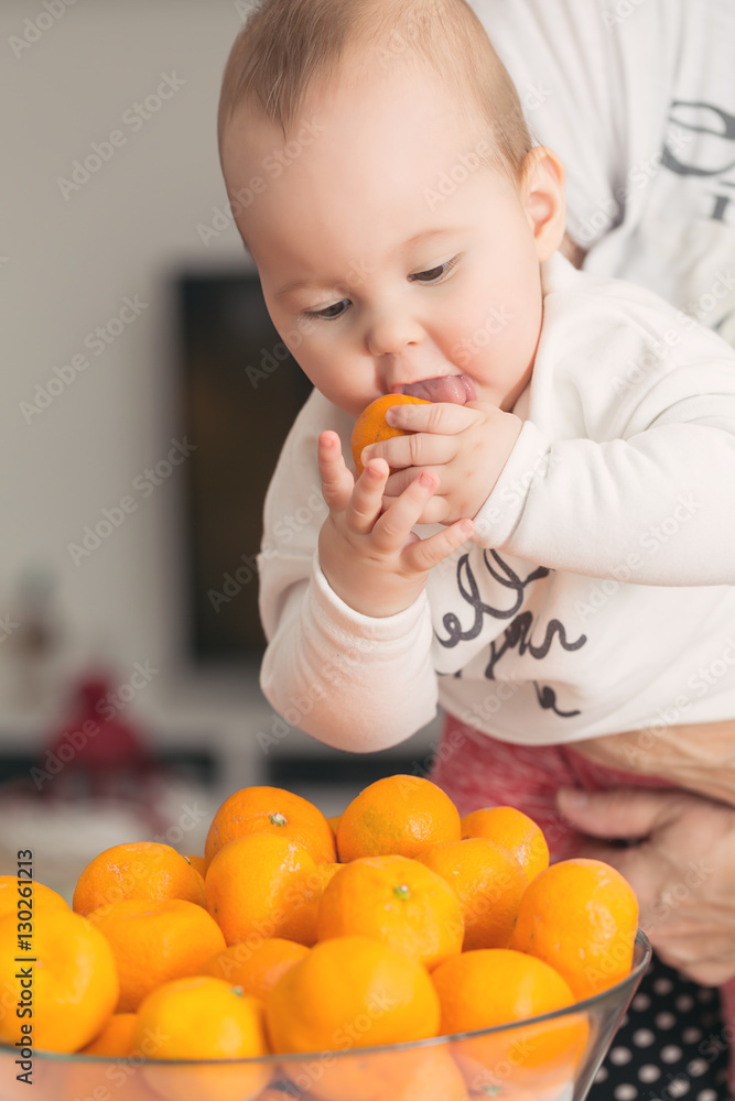 Wall mural Eight months old baby girl sucking a tangerine taken from the bo