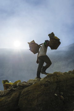 Backlit image of workers loaded with sulphur pieces cut out from a sulphur mine on Ijen crater lake, Java, Indonesia
