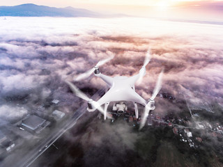 Hovering drone taking pictures of town covered by mist, sunrise