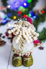 Obraz premium гном, маленький человек, игрушка на белом деревянном столе на фоне новогодней зеленой гирлянды и новогодних разноцветных огней