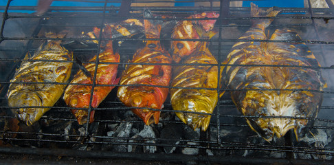 Several bright exotic fish are fried on a brazier and the smoke enveloped them on all sides (Indonesia)