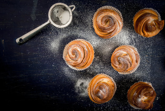 Modern fashionable pastries - scones cruffins  (puffmaffin), a mixture of a croissant and maffin. On blue dark wooden table, sprinkled with powdered sugar. Copy space