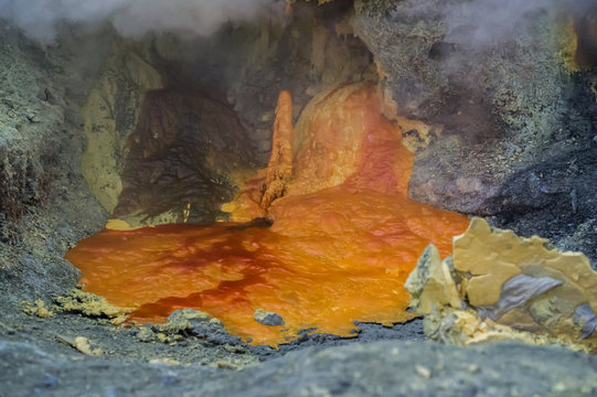 Orange hot lava flows and form puddles on the solidify stone, shrouded in smoke and steam (Indonesia)