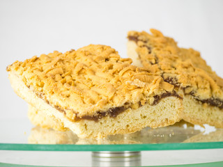 Grated pie with fruit jam on a glass stand, isolated on white