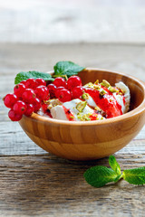 Ice cream with berry sauce and pistachios in a wooden bowl.