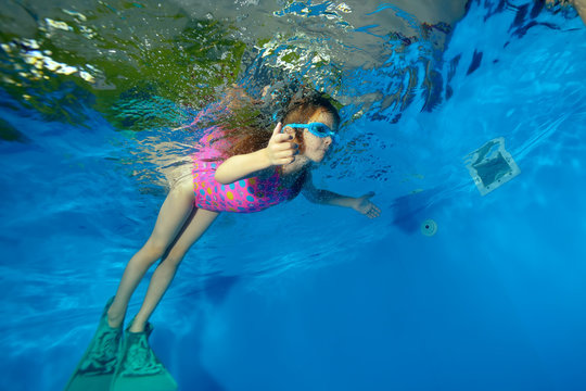 Sports little girl swimming fins underwater in the pool on a blue background. Portrait. The view from under the water at the bottom. Landscape orientation