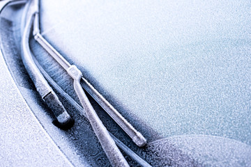 Car windshield and wipers covered with morning frost. Winter contrast background