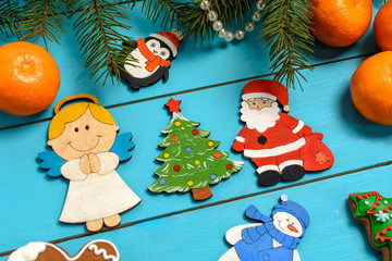 Handmade wooden Christmas tree decorations (Santa, Angel, penguin, rooster, Christmas tree, snowman) on a blue vintage table with Christmas tree and children's toys, tangerine, cakes. 