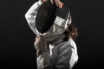 Side view portrait of woman wearing white fencing costume. She puts protective mask on her head.