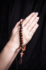 Rosary and cross in female hands on a dark background 