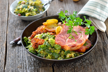 Deftiger geräucherter Kasslernacken mit Speck-Wirsing und Bratkartoffeln in der rustikalen Eisenpfanne serviert - Smoked neck of pork with savoy cabbage, bacon and fried potatoes served in an iron pan