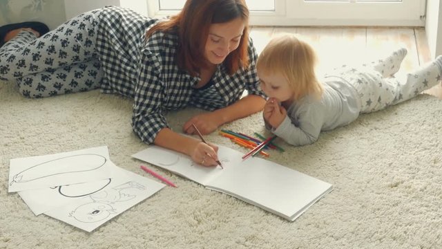 Baby girl with mother draws in album with pencils