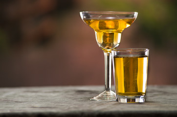 Classy cocktail glass sitting on grey surface, yellow liquid inside with blurry urban background
