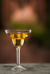 Classy cocktail glass sitting on grey surface, yellow liquid inside with blurry urban background