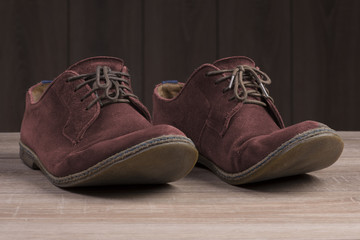 Red suede shoes with brown laces on the background of dark natural wood.