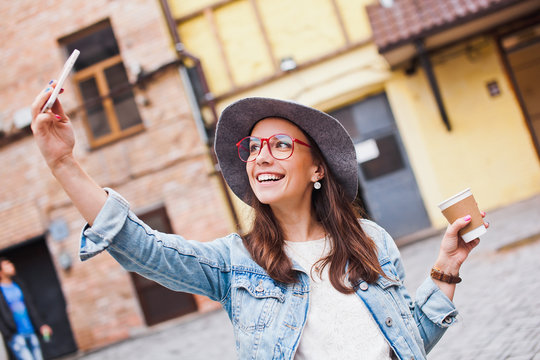 Cheerful young female hipster takes selfie with coffee to go