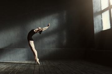 Flexible ballet dancer stretching in the dark lighted studio - obrazy, fototapety, plakaty