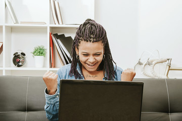 female young african descent with the computer in house celebrating with enthusiasm