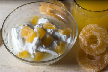 Breakfast with Yogurt with pieces of pineapple and orange juice on a wooden background