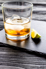 rum with ice in glass on dark background and lime