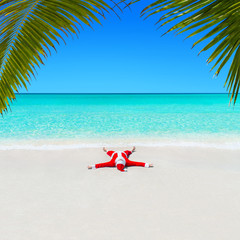 Fototapeta na wymiar Christmas Santa Claus relaxing on sand at ocean palm beach