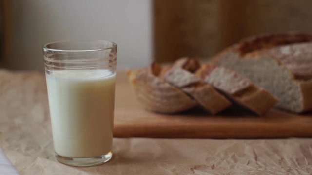 Glass of milk and sliced bread on kitchen table. Dairy product at healthy breakfast. Milk glass and bread slices on cutting board. Milk cup on breakfast table. Breakfast food at morning