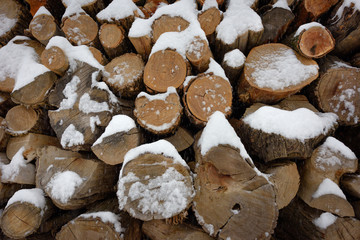 Faces of logs in winter. Woodpile of firewood under snow. Abstract background texture.