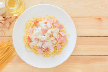Spaghetti carbonara with chopped bacon, cheese sauce and checkered towel on white dish over wooden table background, Top view with copy space and text.