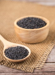 Close up black sesame in bowl and spoon on wooden plank