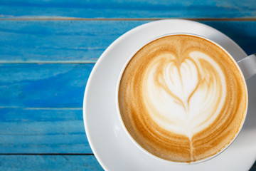 Top view hot latte coffee in white cup on blue vintage wooden ta
