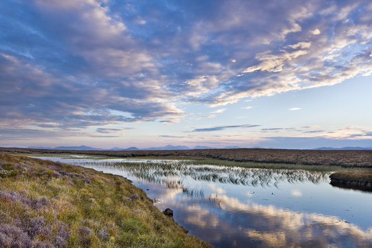Evening reflections in a lochan on the peaty moreland of Lewis, with the mountains of Harris in the distance, Isle of Lewis, Outer Hebrides, Scotland