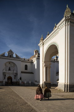 Traditionally dressed women walking past Copacabana Cathedral after dawn, Copacabana, Lake Titicaca, Bolivia