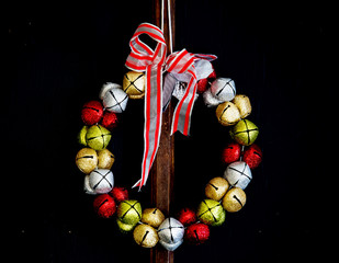 A red, silver, gold and green jingle bell Christmas wreath on a black background