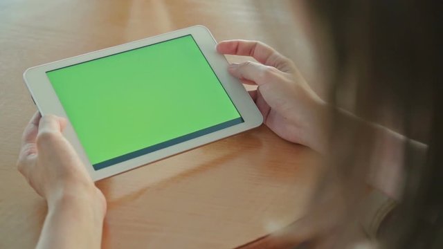 Woman looking at tablet computer with green screen in cafe. Close up shot of woman's hands with pad