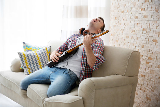 Young man in headphone enthusiastically playing the electric guitar in a light room